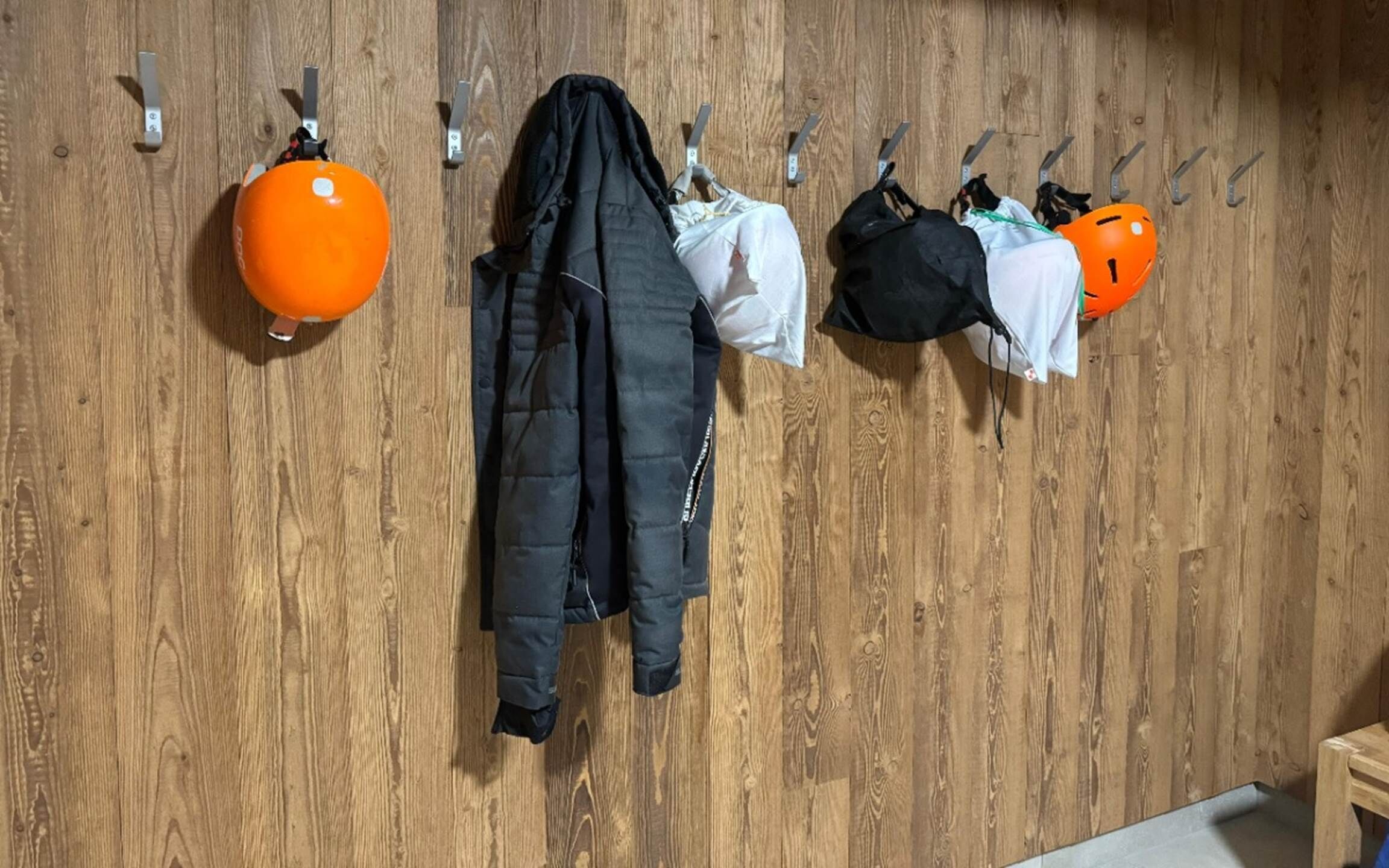 Een houten wand met meerdere haken waarop onder meer jassen, een helm en een rond oranje object hangen.