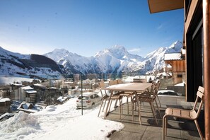 Paesaggio montano innevato con vista su una cittadina e un balcone con tavolo e sedie.