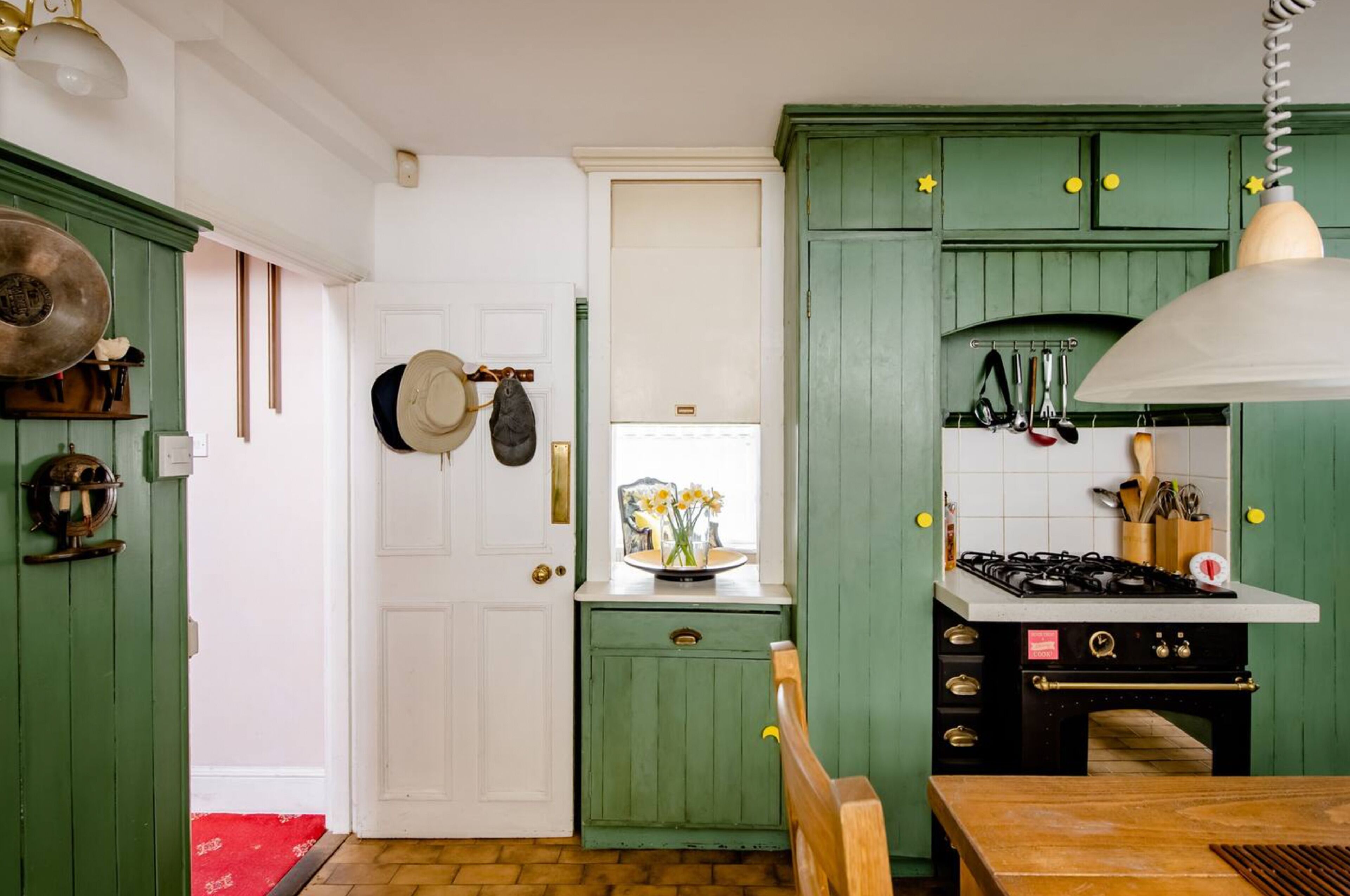 Una cocina con armarios verdes, una puerta blanca y una estufa.
