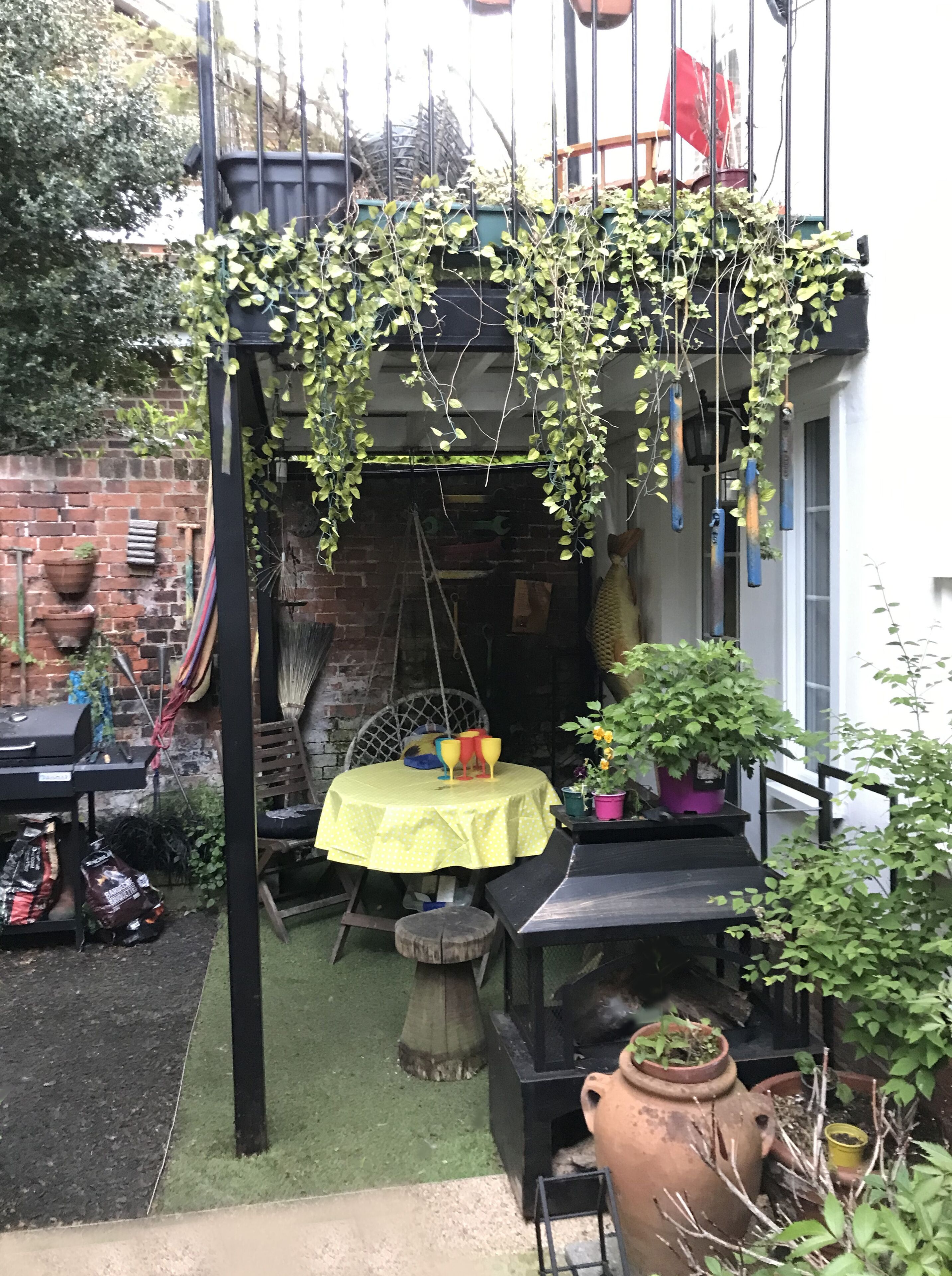A patio area with a table set for four, surrounded by potted plants and a hanging plant arrangement.