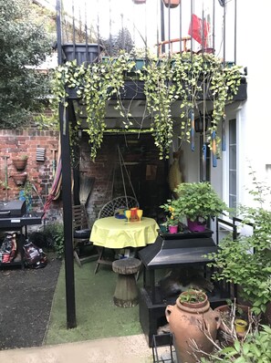 A patio area with a table set for four, surrounded by potted plants and a hanging plant arrangement. - Billericay Georgian House, Sleeps 6 - Pet Friendly (Billericay)
