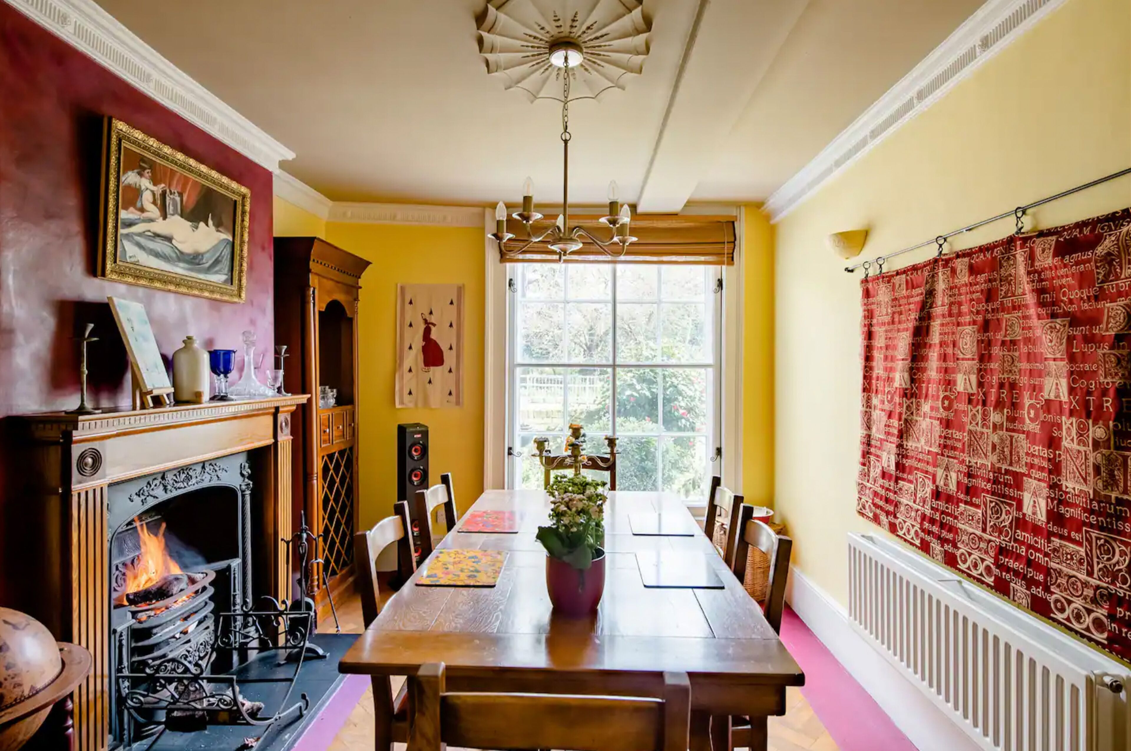 A dining room with a fireplace, a chandelier, and a large window with a view of trees.