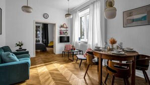 Un salon moderne avec un canapé, une table à manger et des chaises. Il y a un téléviseur accroché au mur et une horloge.
