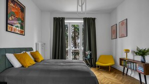 Une chambre à coucher avec un lit, une chaise, une table de chevet et une fenêtre avec des rideaux.