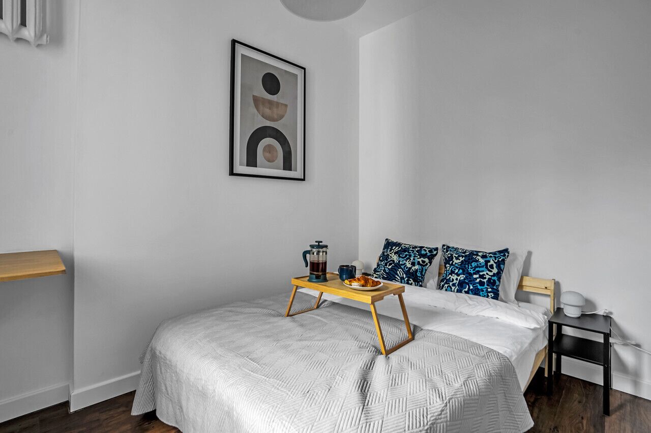 Une chambre à coucher bien rangée, avec un lit, une table de chevet et une petite étagère.