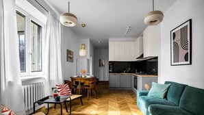 Un salon moderne avec un parquet en chevrons, un canapé de couleur turquoise et un coin repas comprenant une table et des chaises en bois.