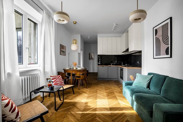 A modern living room with a herringbone floor, a teal sofa, and a dining area with a wooden table and chairs.