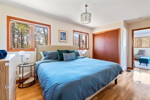 Cozy bedroom with a large bed and ceiling fan, featuring two windows and a wooden door.