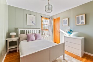 Cozy retreat with a comfortable bed, nightstand, and globe, set against a serene backdrop of framed artworks.