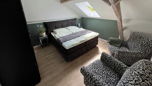 Et soveværelse med skrå væg, ovenlys, seng med gavl, natbord med lampe og møbler med mønster.
