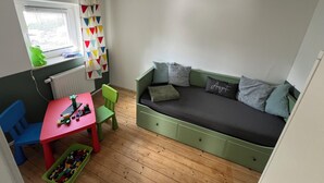 Et børneværelse med en grøn sofa, et rødt bord og et vindue med skodder.