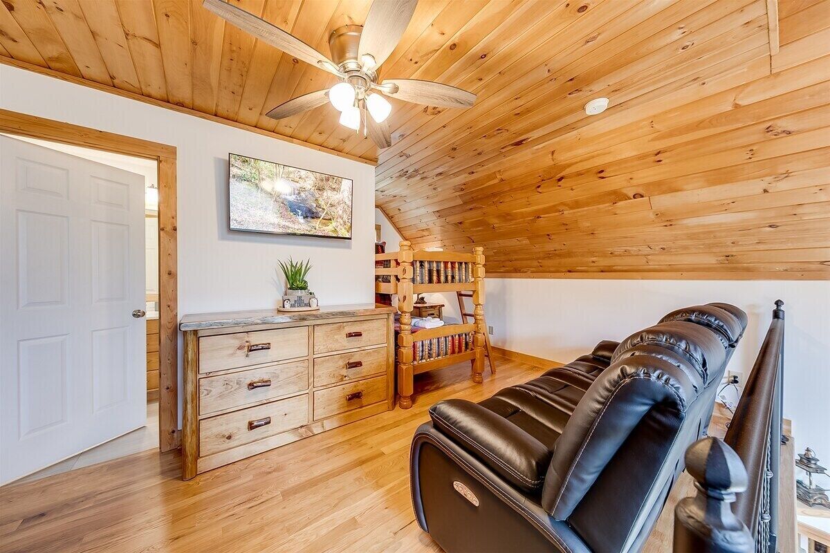 Una habitación con techo de madera, ventilador de techo, sofá de cuero negro, estantería de madera y puerta blanca.
