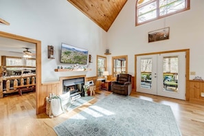 A spacious living room with a fireplace, wooden floors, a large rug, and a ceiling fan. - Waterfall Cabin/ 2 BR in Helen| private waterfall (Sautee Nacoochee)