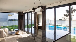 A modern living room with a glass wall, a pool, and a view of the outdoors.