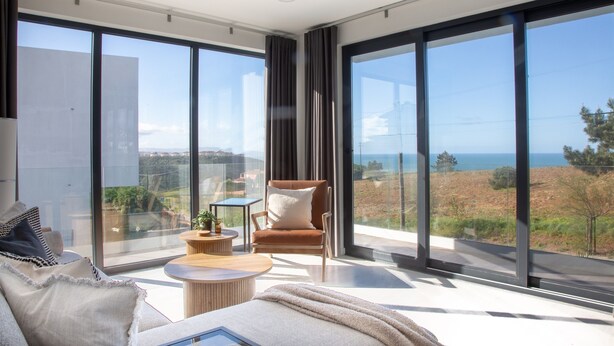 A modern living room with large glass windows, a sofa, a chair, and a small table.