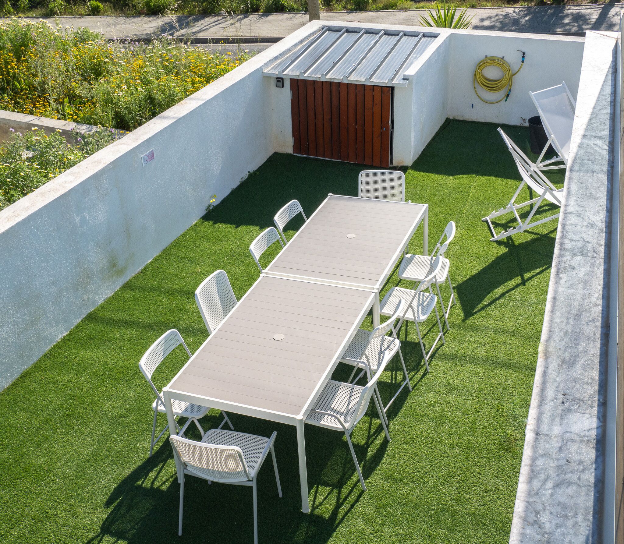 A rooftop patio with a rectangular table and six chairs, surrounded by artificial grass.