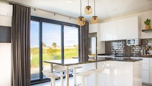 A modern kitchen with a large island, white bar stools, and a view of the outdoors.