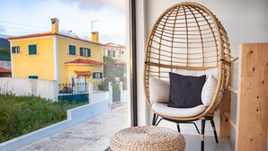 Ein Zimmer mit großem Fenster, einem Korbstuhl mit Kissen und einer Holztür.