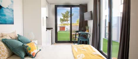 A hotel room with a bed, a TV, a balcony with a table and chairs, and a view of the outdoors.