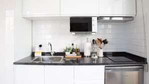 Una cocina moderna con armarios blancos, un lavamanos de acero inoxidable, un microondas y un lavavajillas.