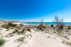 A sandy beach with a wooden fence leading to the water, clear skies, and distant buildings. - 3835 Summer House by Barbarhouse (Porto Cesareo)