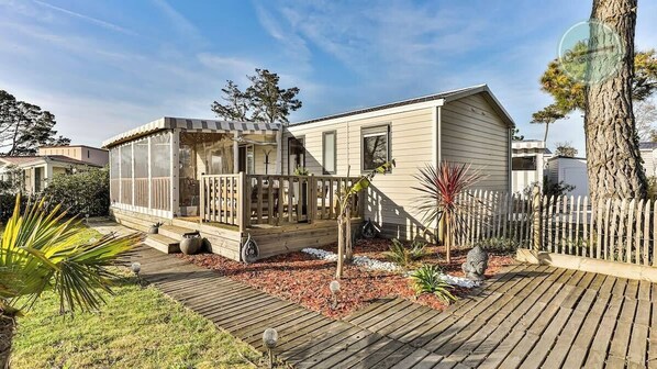 A mobile home with a deck, surrounded by a wooden fence and various plants.