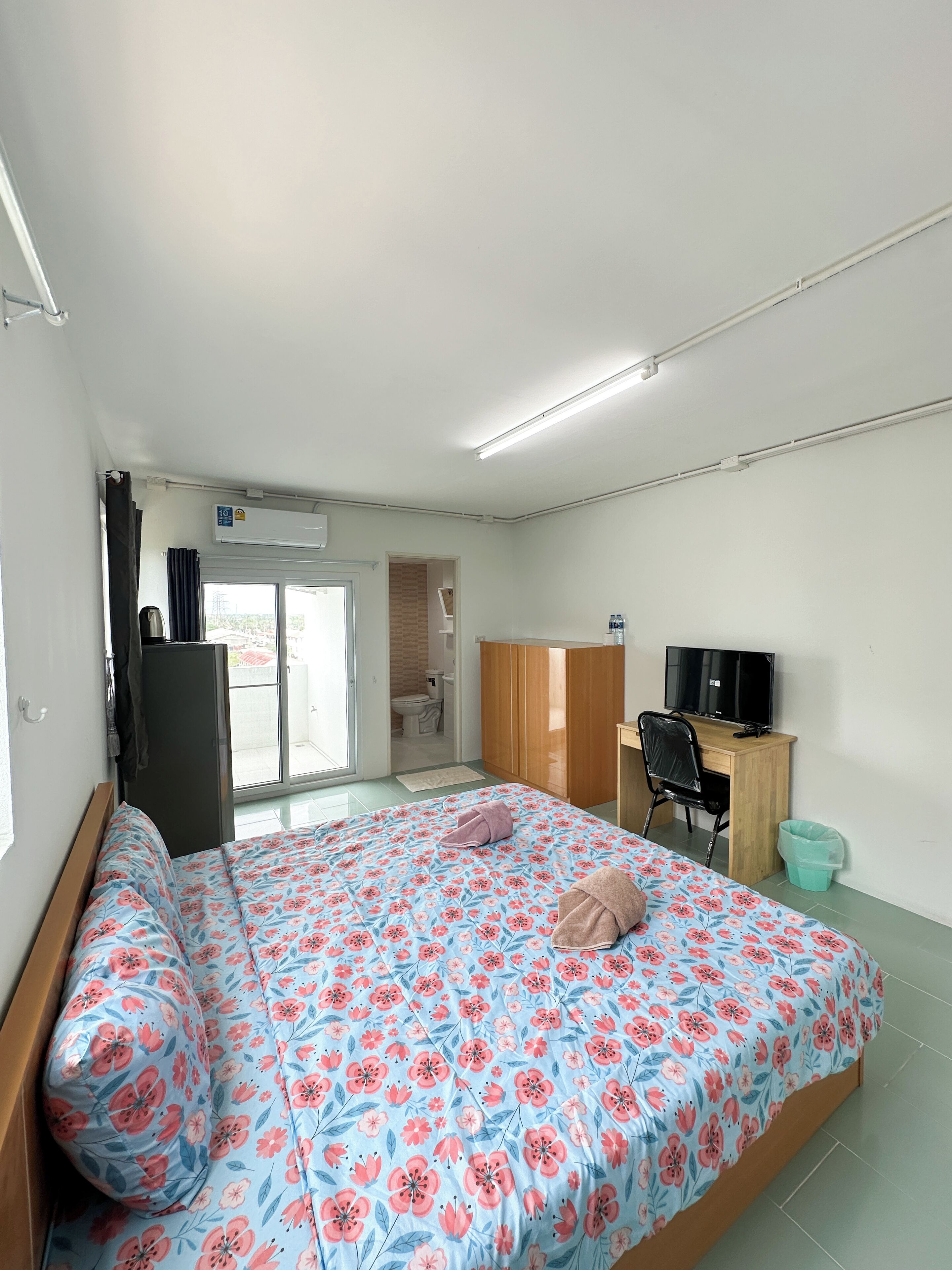 A bedroom with a bed, a desk, a TV, and a bathroom visible through an open door.