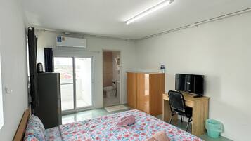 A bedroom with a bed, a desk, a TV, and a bathroom visible through an open door.