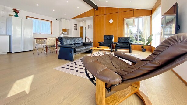A modern living room with a leather sofa, a reclining chair, and a dining area with a table and chairs. - Waterfront villa near IKEA and Sylvia Park (Auckland)