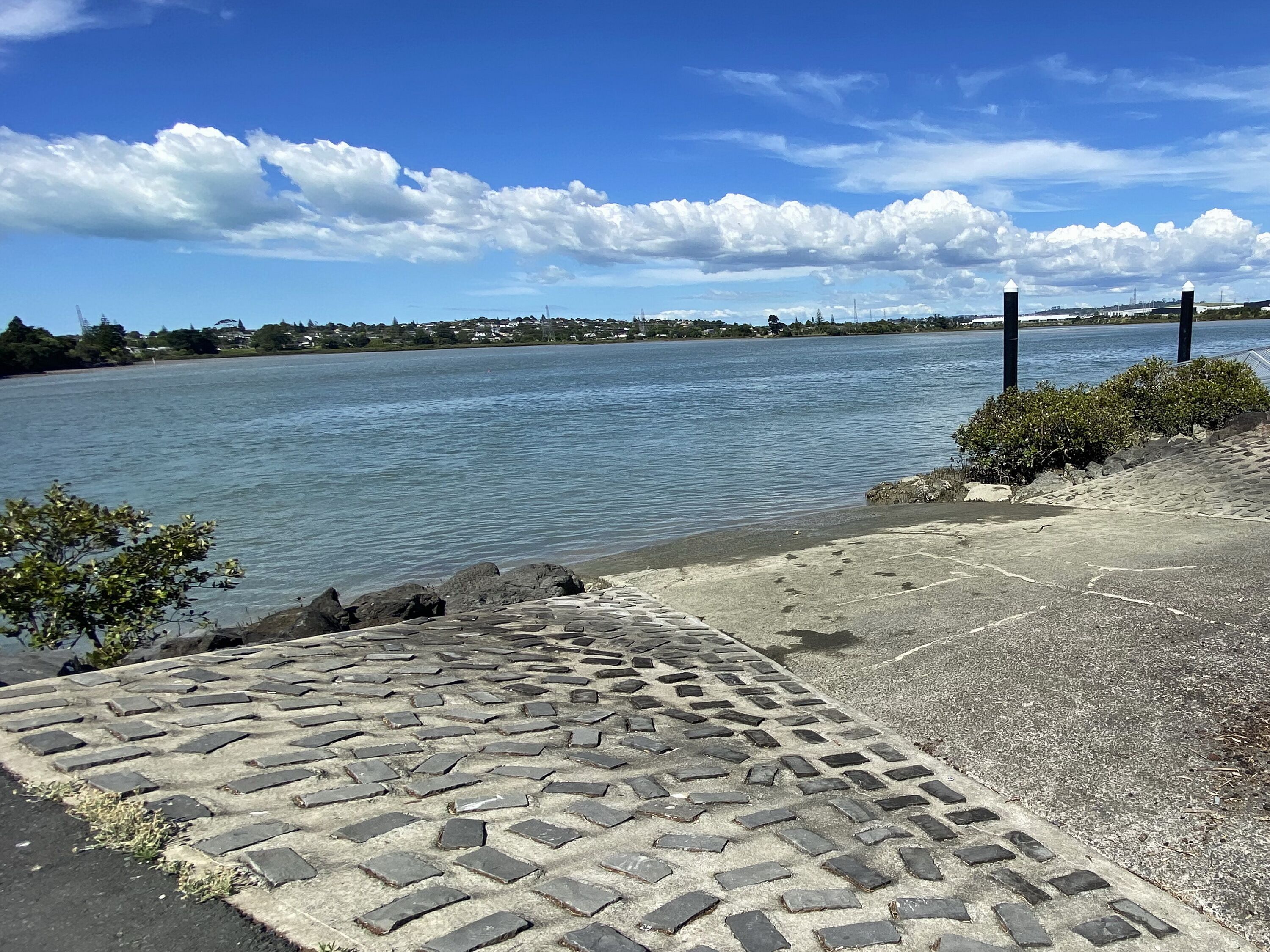 Un camino pavimentado que conduce a la orilla con vista clara al agua y edificios distantes.