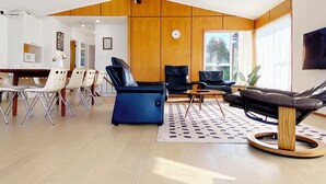 A modern living room with a dining area, featuring a wooden ceiling, a large window, and a flat-screen TV. - Waterfront villa near IKEA and Sylvia Park (Auckland)