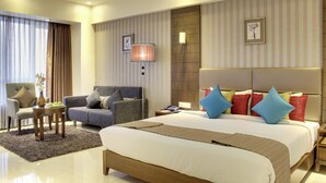 A hotel room with a large bed, a sofa, a chair, a small table, and a lamp. - The Radiant Swan (Vagra)