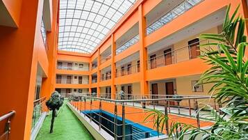 Un atrio de varios niveles con techo de vidrio, una piscina central y césped artificial verde.