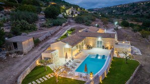 A villa with a swimming pool, stone walls, and a well-lit outdoor area. - Villa Domus Sicilia - Charming Living (Modica)