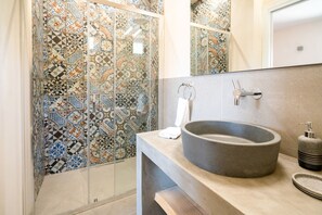 A bathroom with a tiled shower wall, a round sink, and a mirror above the sink. - Villa Domus Sicilia - Charming Living (Modica)