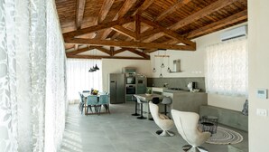 A spacious kitchen with modern appliances, a dining area with light blue chairs, and a high wooden ceiling. - Villa Domus Sicilia - Charming Living (Modica)