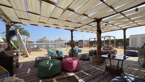 An outdoor seating area with colorful bean bags and a striped rug, overlooking a beach with umbrellas and a clear sky. - Sharm Hills Aqua park Resort (Sharm El Sheikh)