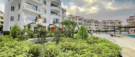 A hotel with multiple balconies, a swimming pool, and lush greenery.