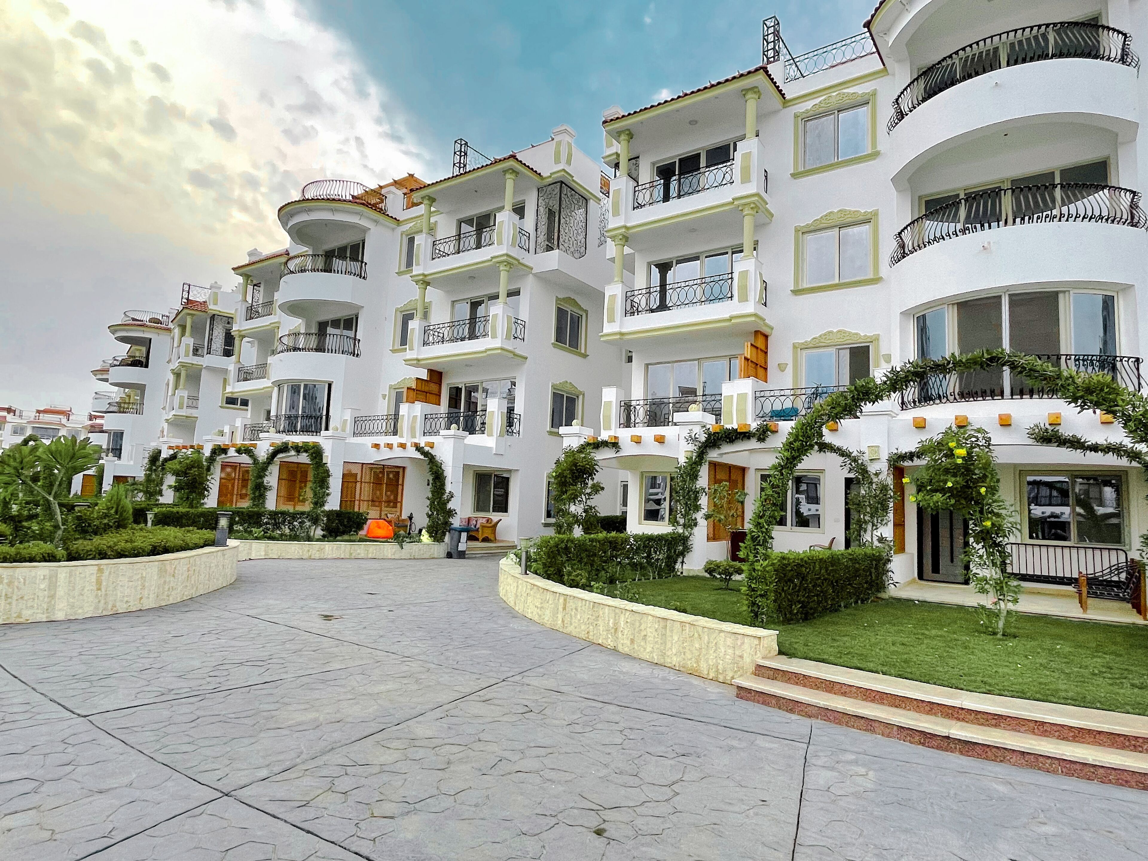 Edifici residencial de diverses plantes amb balcons, un pati pavimentat i vegetació.