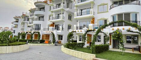 Edifici residencial de diverses plantes amb balcons, un pati pavimentat i vegetació.