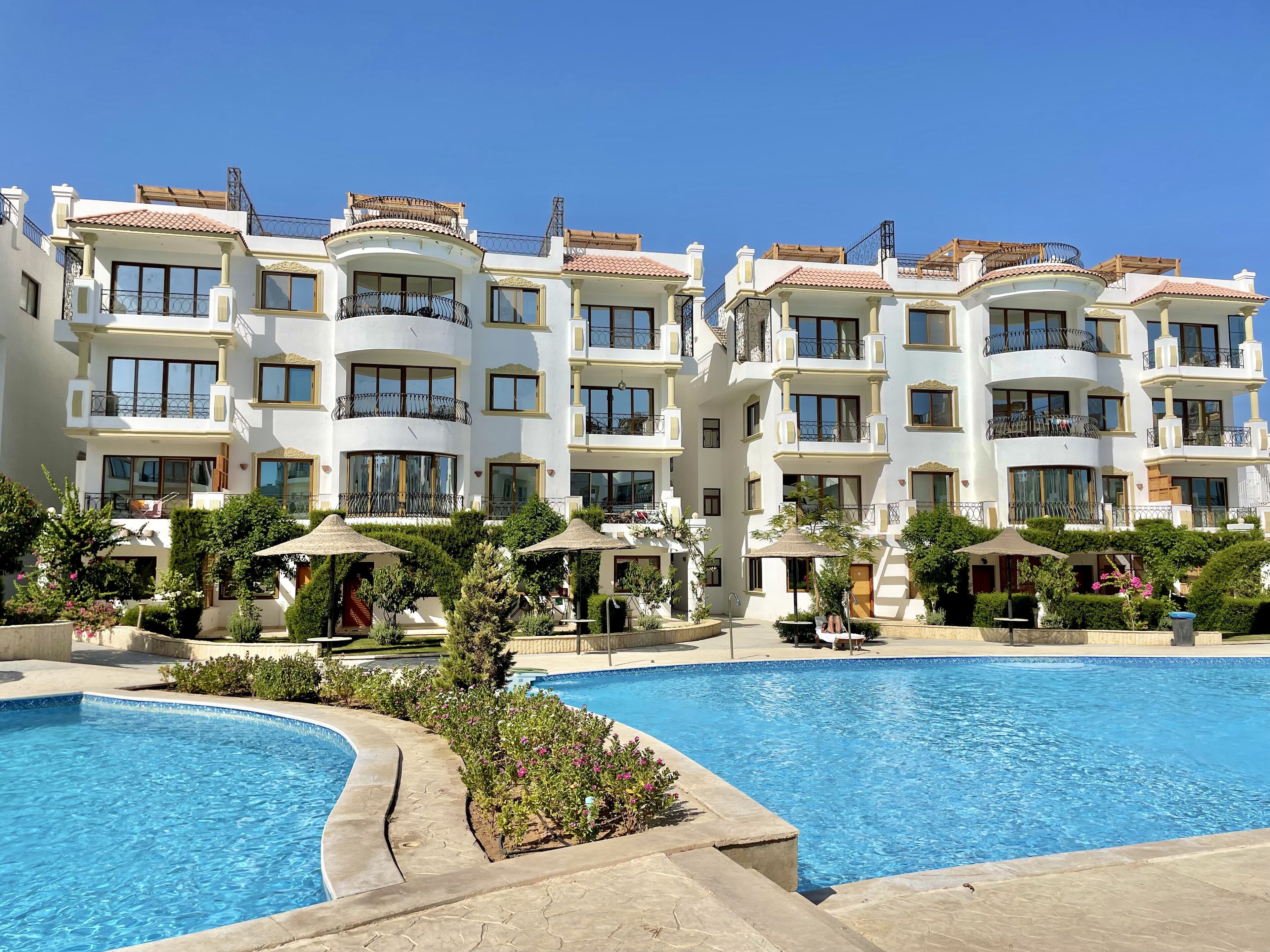 A multi-story hotel with balconies, a swimming pool, and outdoor seating areas.