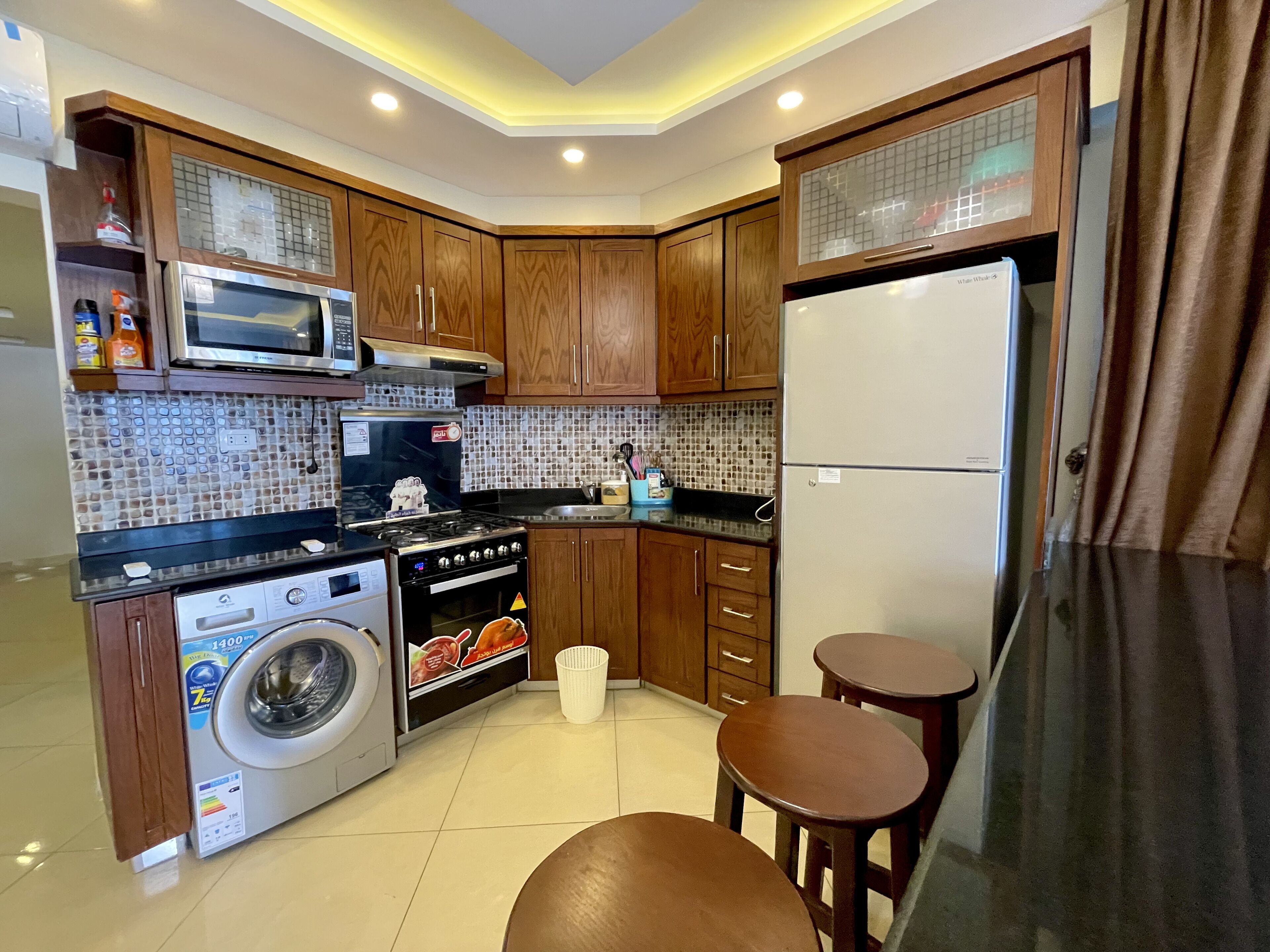 Una cocina compacta con armarios de madera, microondas, estufa, lavadora y refrigerador.