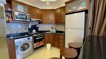 Una cocina compacta con armarios de madera, microondas, estufa, lavadora y refrigerador.