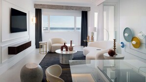 A modern hotel room with a large TV, comfortable seating, a round coffee table, and a view of the sea. - Blue Marina Suites Boutique Apartments (Arrecife)