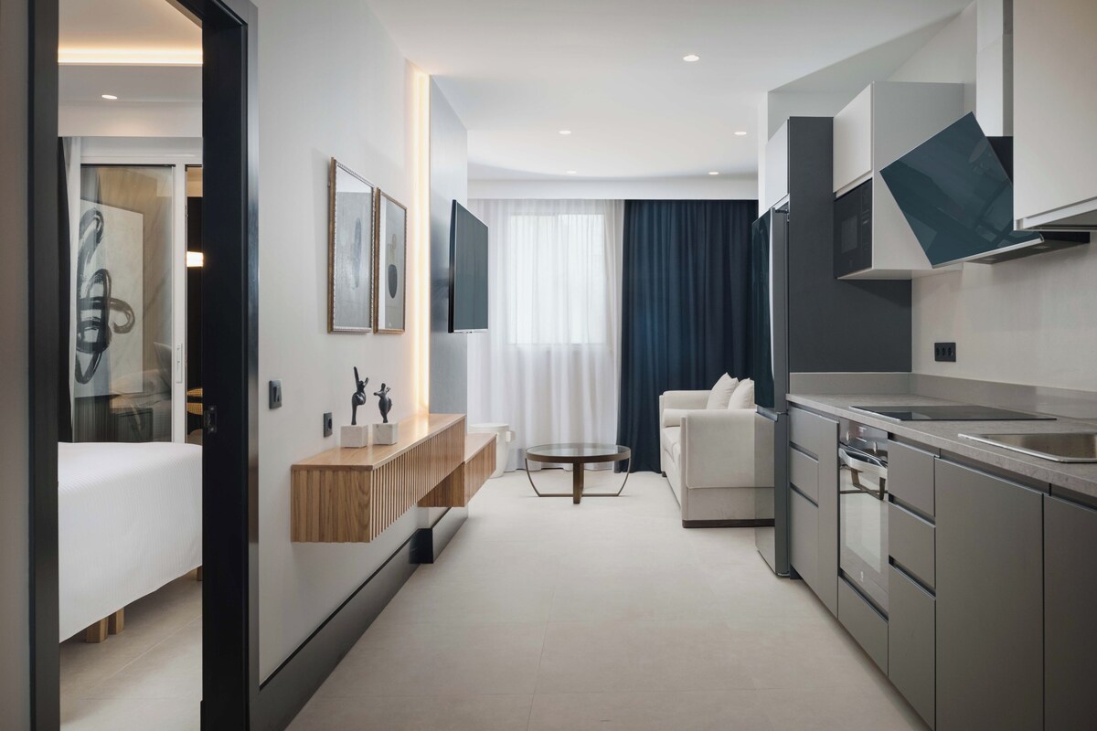 Une chambre d’hôtel moderne comprenant un lit, un petit coin salon, une kitchenette et une salle de bain.