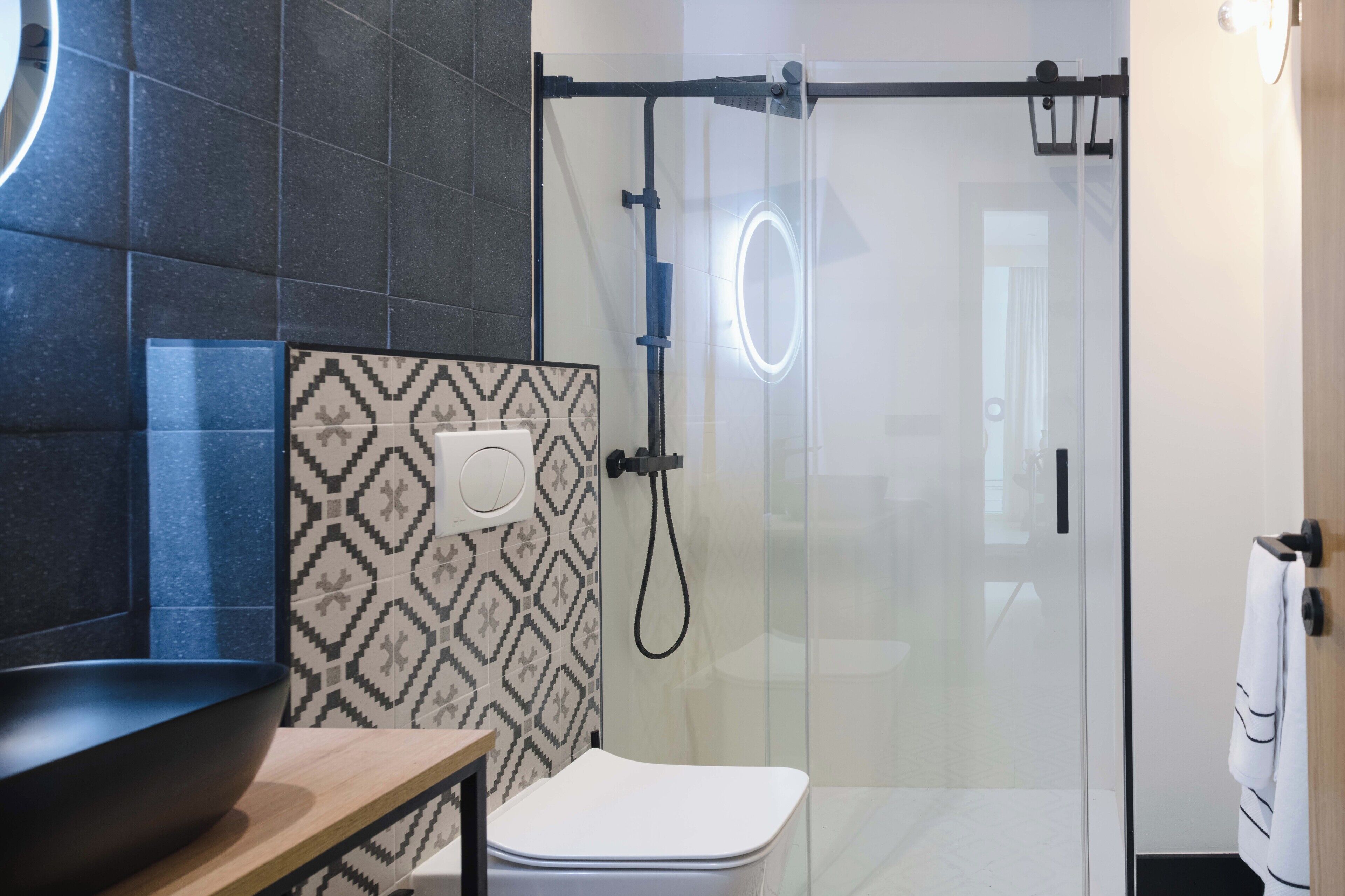 A modern bathroom with a glass shower enclosure, a black sink, and patterned tiles.