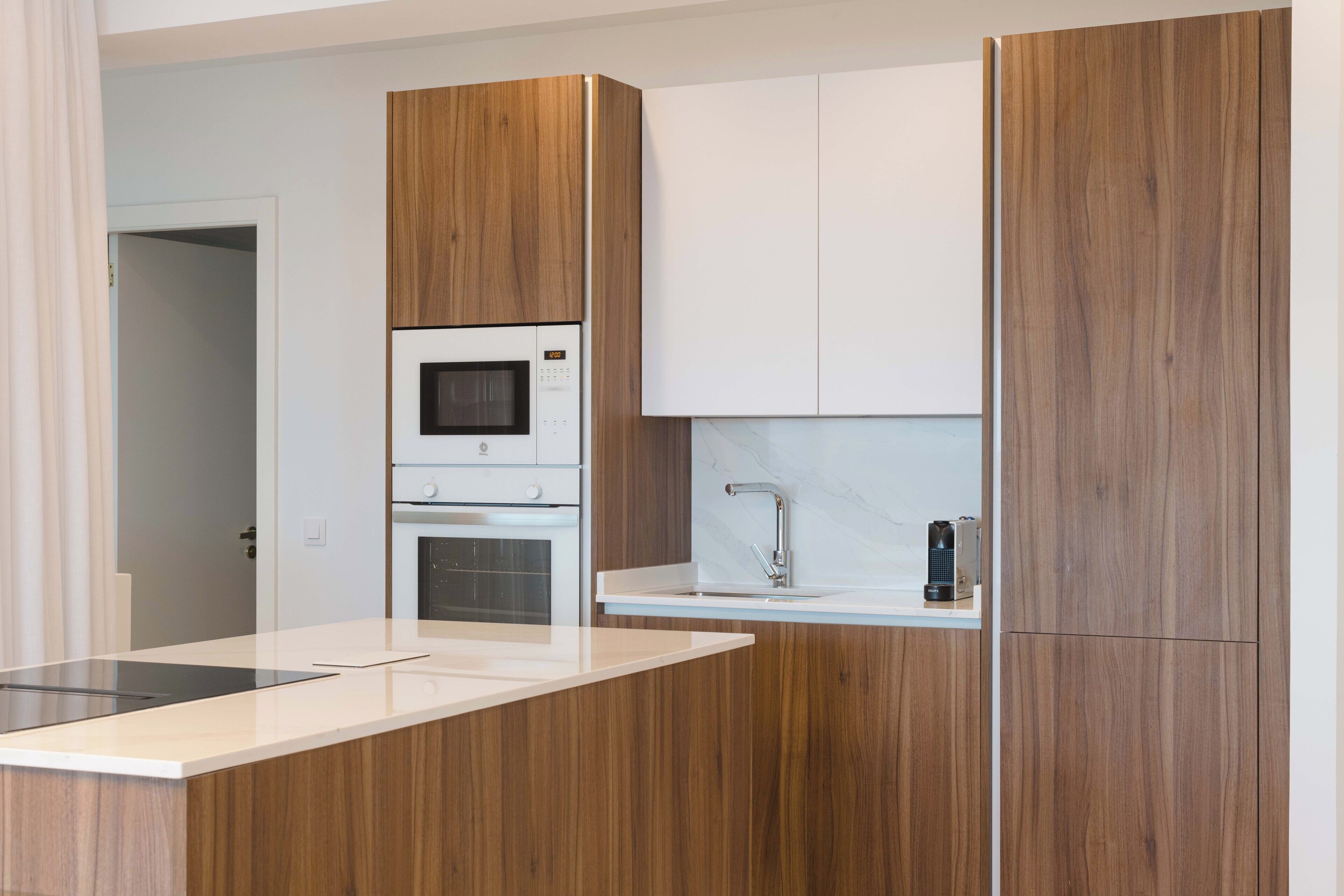 Una cocina moderna con armarios de madera, microondas integrado, horno y un lavamanos con grifo.