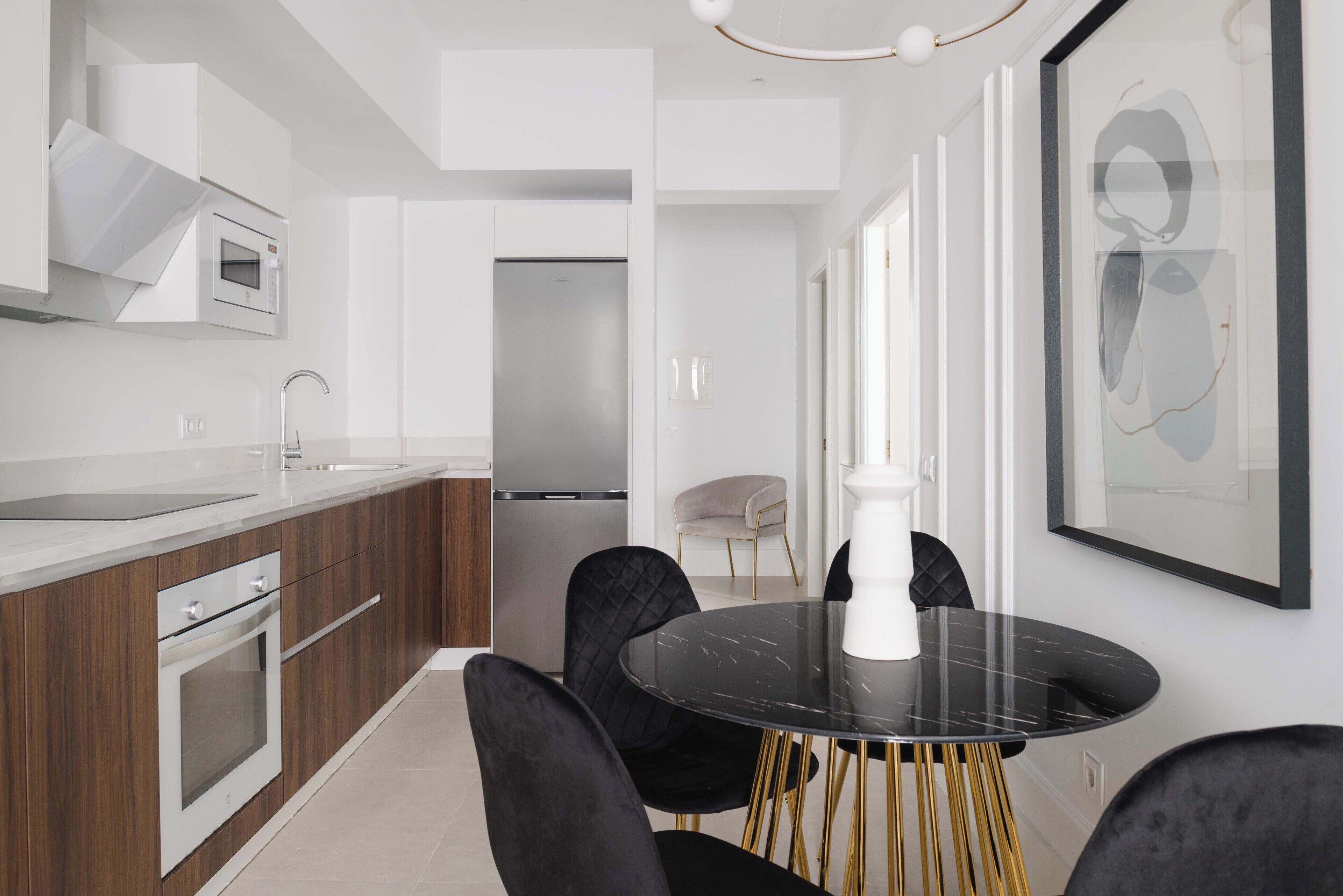 Una cocina moderna con una mesa de mármol negro, sillas doradas y una lámpara colgante blanca.