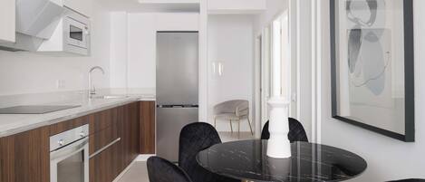 Una cocina moderna con una mesa de mármol negro, sillas doradas y una lámpara colgante blanca.