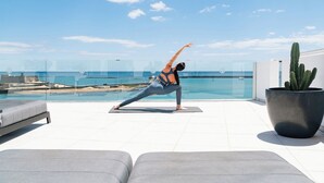 A person performing a yoga pose on a mat with a pool and beach view. - Blue Marina Suites Boutique Apartments (Arrecife)